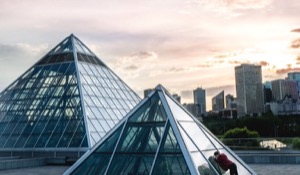 Edmonton muttart conservatory roof with person peeking in the pyramid roof window with edmonton in the background and the sun setting in the distance