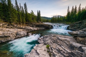 Mountain river cascading down small waterfalls at dawn with rocky mountains in the background